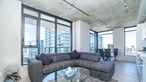 Una sala de estar moderna con un sofá seccional, una mesa de centro de vidrio y ventanas amplias con vistas a la ciudad.