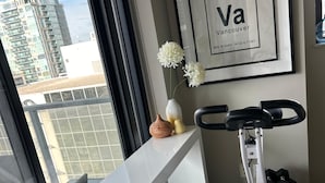 A modern room with a white desk, an exercise bike, and a vase with flowers. A framed map of Vancouver is on the wall.