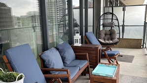 A modern outdoor seating area with a sofa, chairs, and a hanging chair, featuring a city view through large windows.