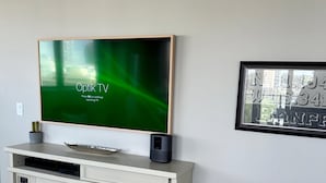 A modern living room with a flat-screen TV on a white entertainment unit, a framed picture on the wall, and a small speaker.