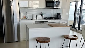 A modern kitchen with white cabinetry, stainless steel appliances, and a central island with stools.