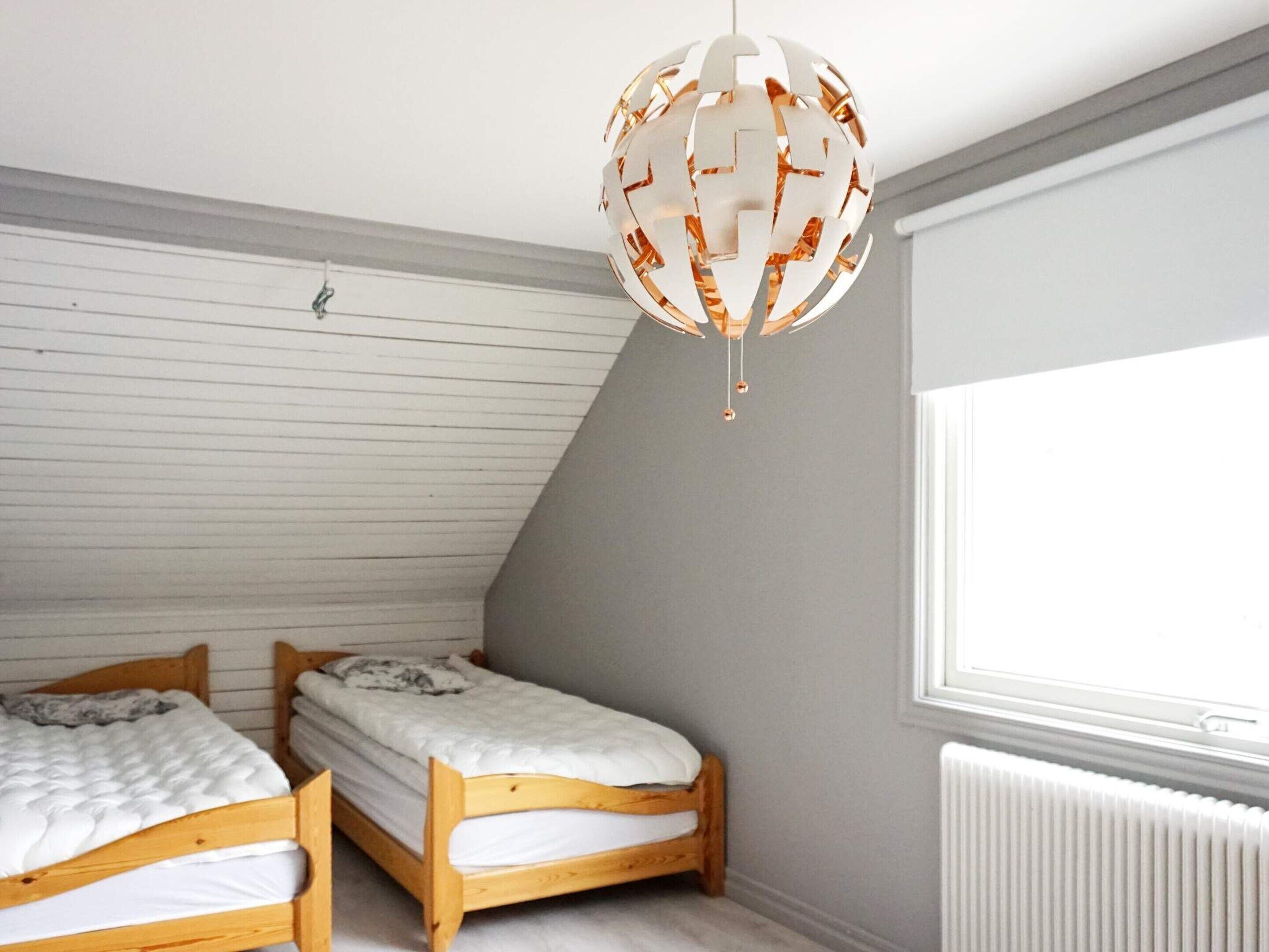 A room with two wooden bunk beds, a white radiator, and a large window providing natural light.