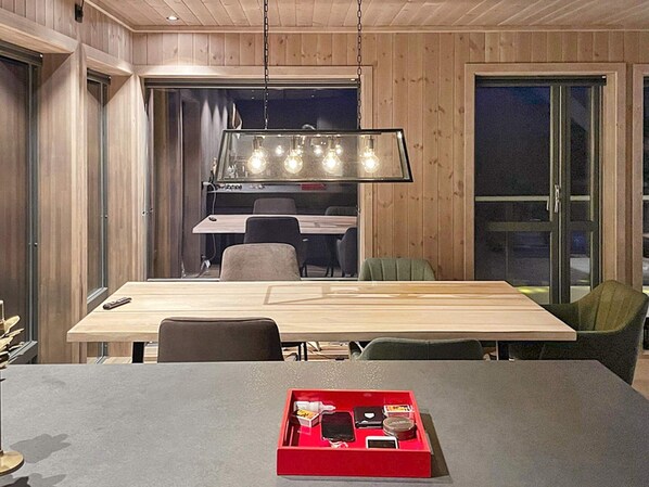 A modern dining area with a wooden table and chairs, a red tray with items, and a hanging light fixture. - 8 Person Holiday Home in Noresund (Krodsherad)