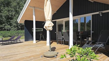 Um deck de madeira com espreguiçadeiras, uma mesa e um guarda-sol.