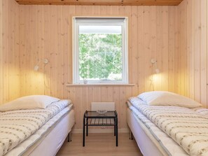 Ein Zimmer mit zwei Betten, einem kleinen Tisch und einem Fenster mit Blick auf Bäume.