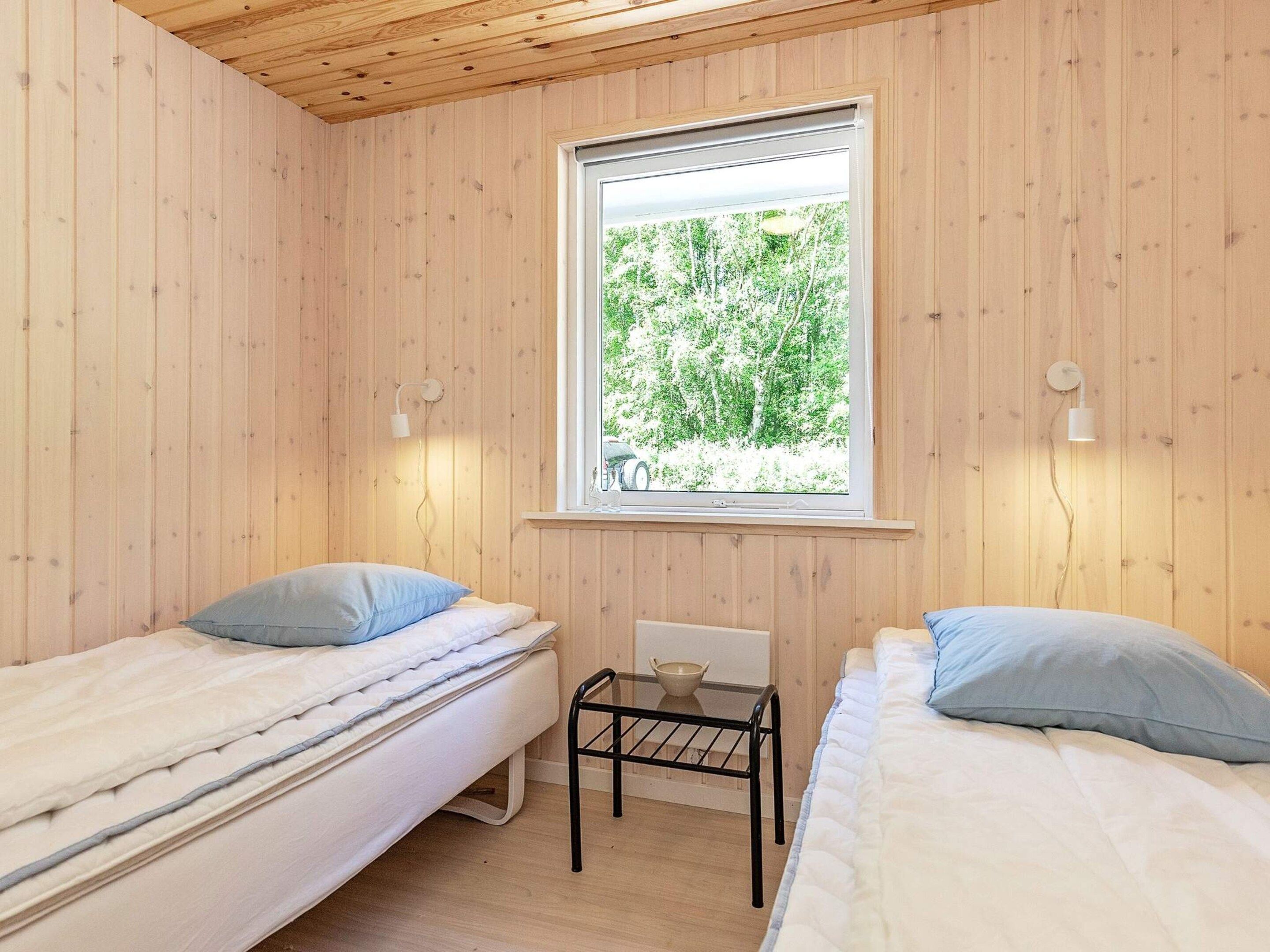 Una habitación pequeña con paneles de madera, dos camas, un ventanal y una mesita.
