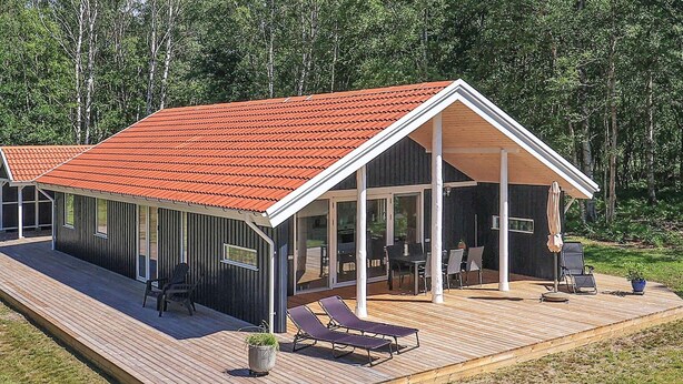 Une maison moderne avec un toit rouge, une terrasse couverte et une plateforme en bois.
