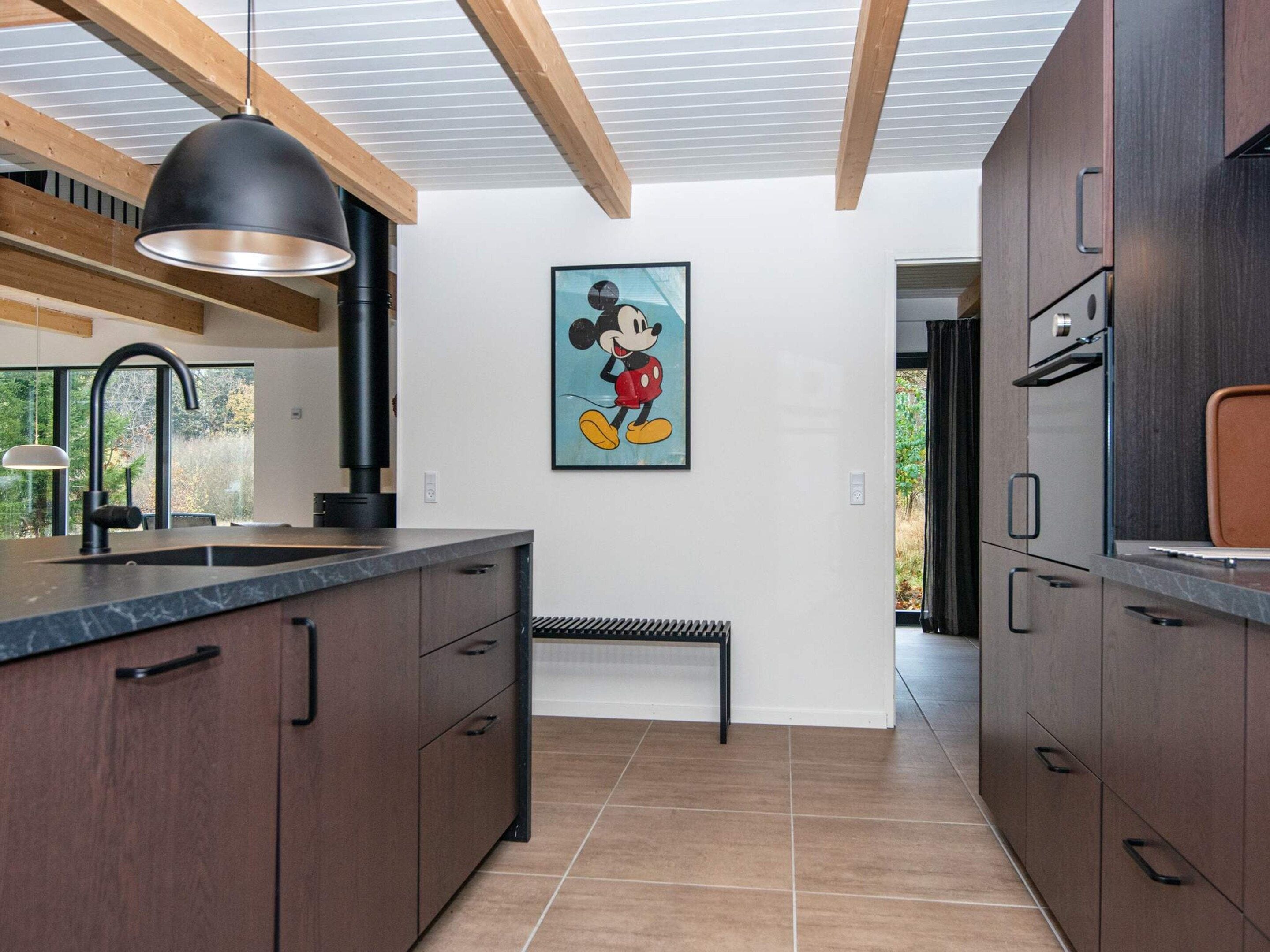 Una cocina moderna con armarios de madera oscura, una lámpara colgante negra y un cuadro de Mickey Mouse en la pared.