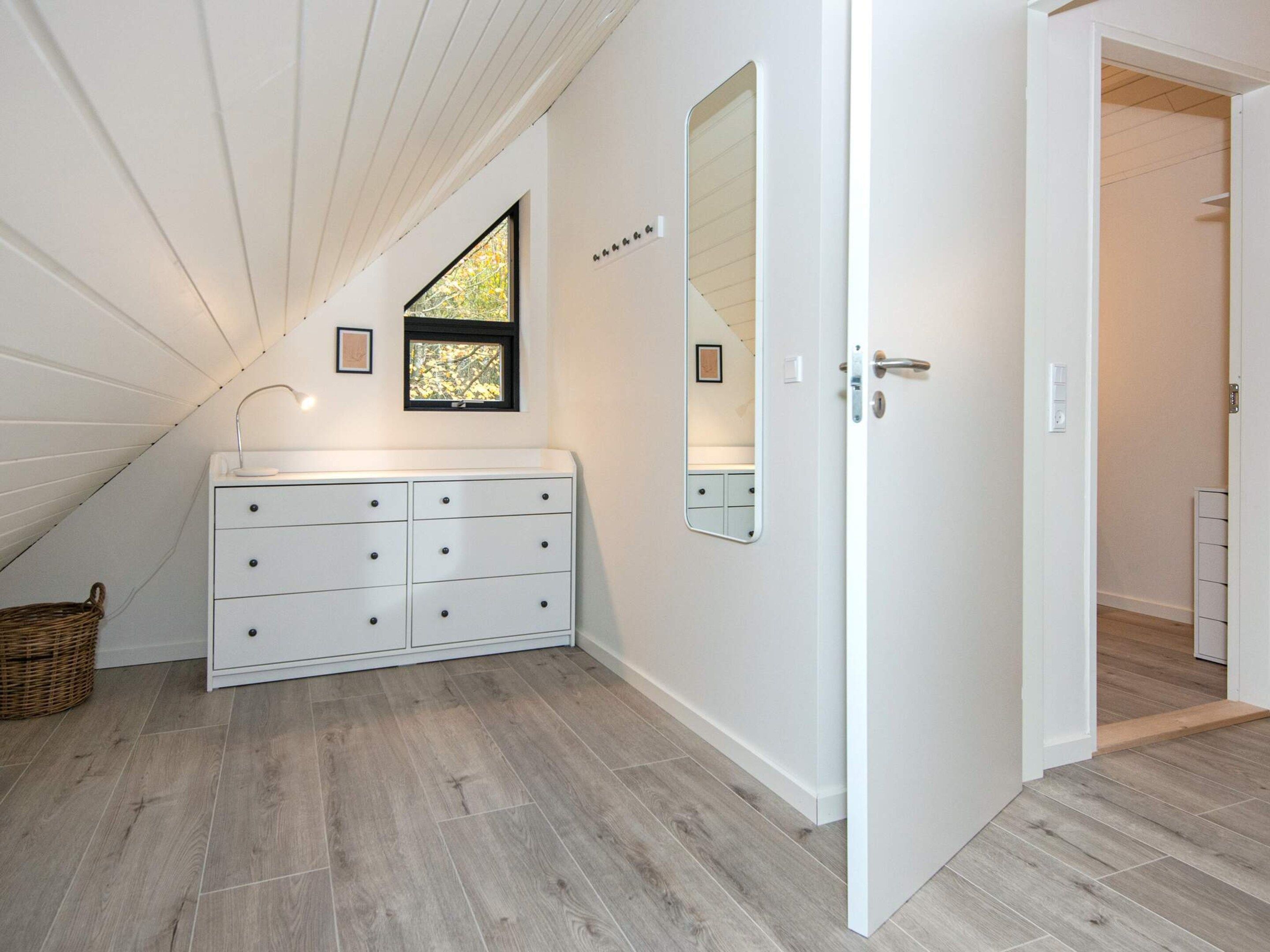 A room with a white vanity, a mirror, a window with a view, and a door leading to another room.