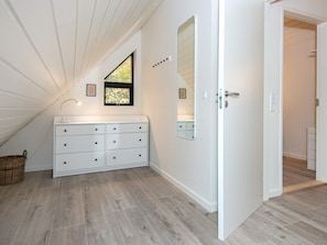 Una habitación con tocador blanco, un espejo, una ventana con vistas y una puerta que da a otra estancia.