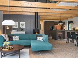 Een moderne woonkamer met een hoekbank, een open haard en een keuken met barstoelen.