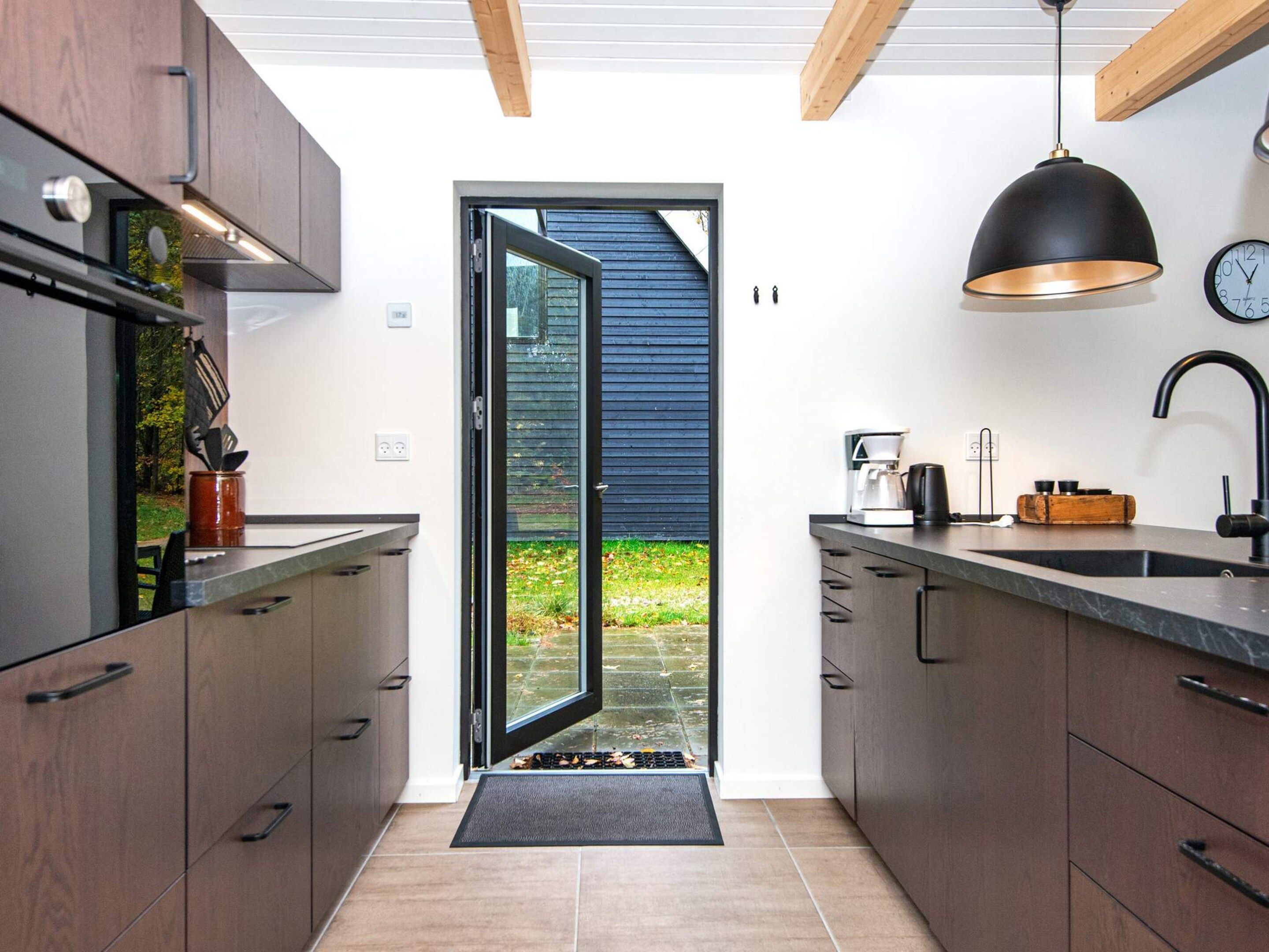 A modern kitchen with dark wood cabinets, a black countertop, a coffee maker, and a black pendant light.
