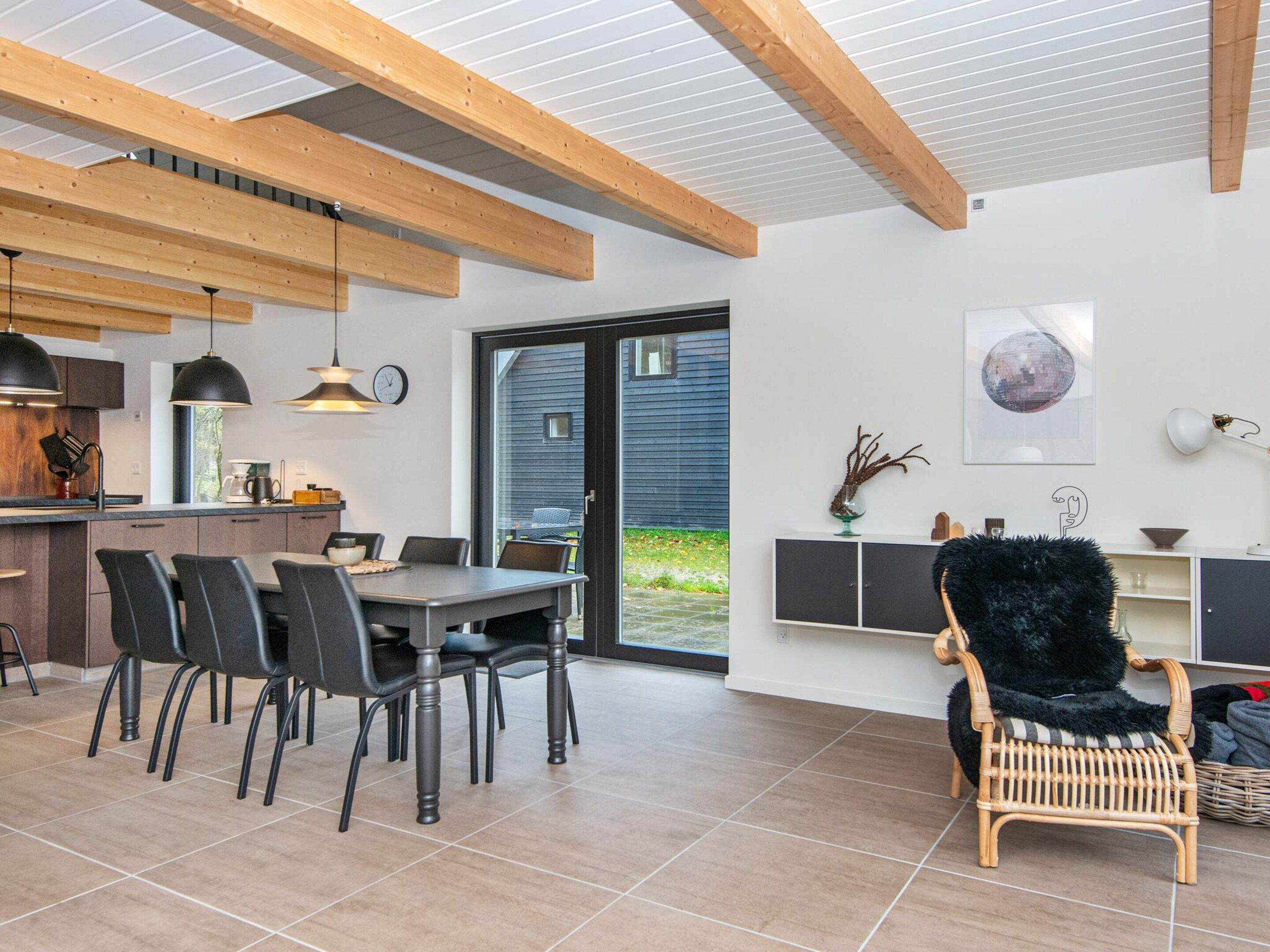 A modern kitchen with wooden beams, a dining area with black chairs, and a large window.
