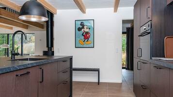 A modern kitchen with dark wood cabinets, a marble countertop, a black pendant light, and a Mickey Mouse painting on the wall.
