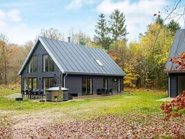 A modern two-story house with a sloped roof, large windows, and a patio area with outdoor furniture.