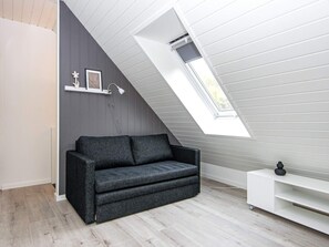 Une chambre de style loft moderne, avec un plafond en pente, un canapé gris, une console blanche et une lucarne.