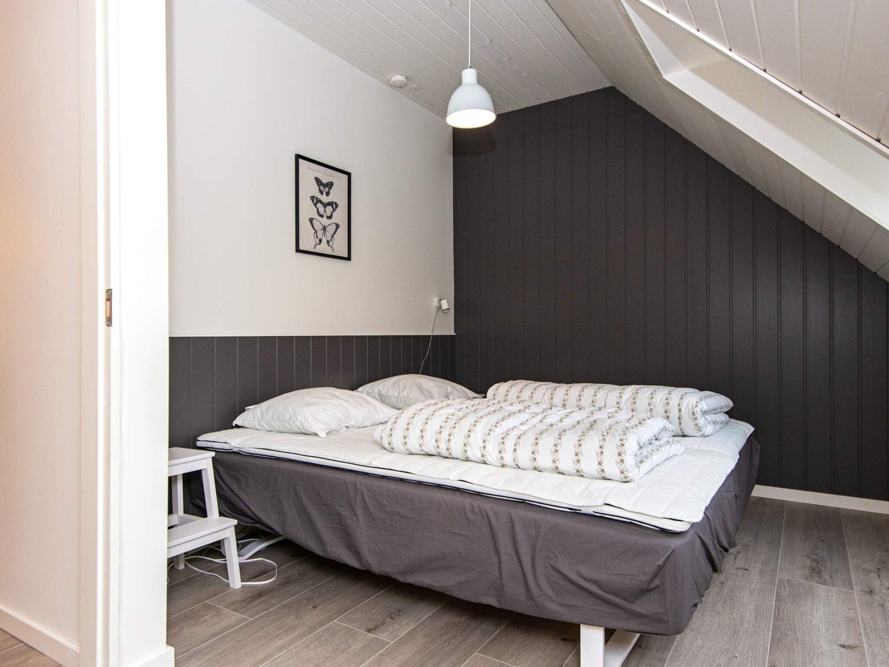 A bedroom with a bed, a bedside table, a hanging light, and a wall-mounted picture.