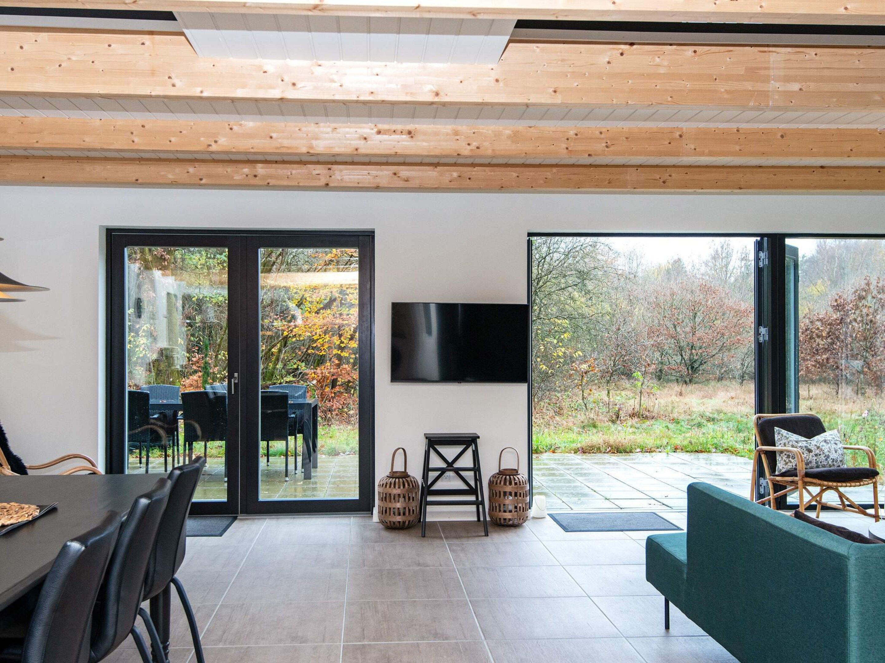 Una sala de estar moderna con comedor, televisor montado en la pared y vistas al exterior a través de amplias puertas de cristal.