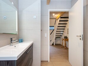 A modern bathroom with a white sink, a mirror, and a wooden cabinet. There is a staircase leading to another room.