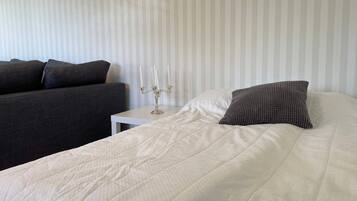 A neatly made bed with a white duvet and a textured pillow, a bedside table with a candelabra, and a dark sofa against a striped wall.