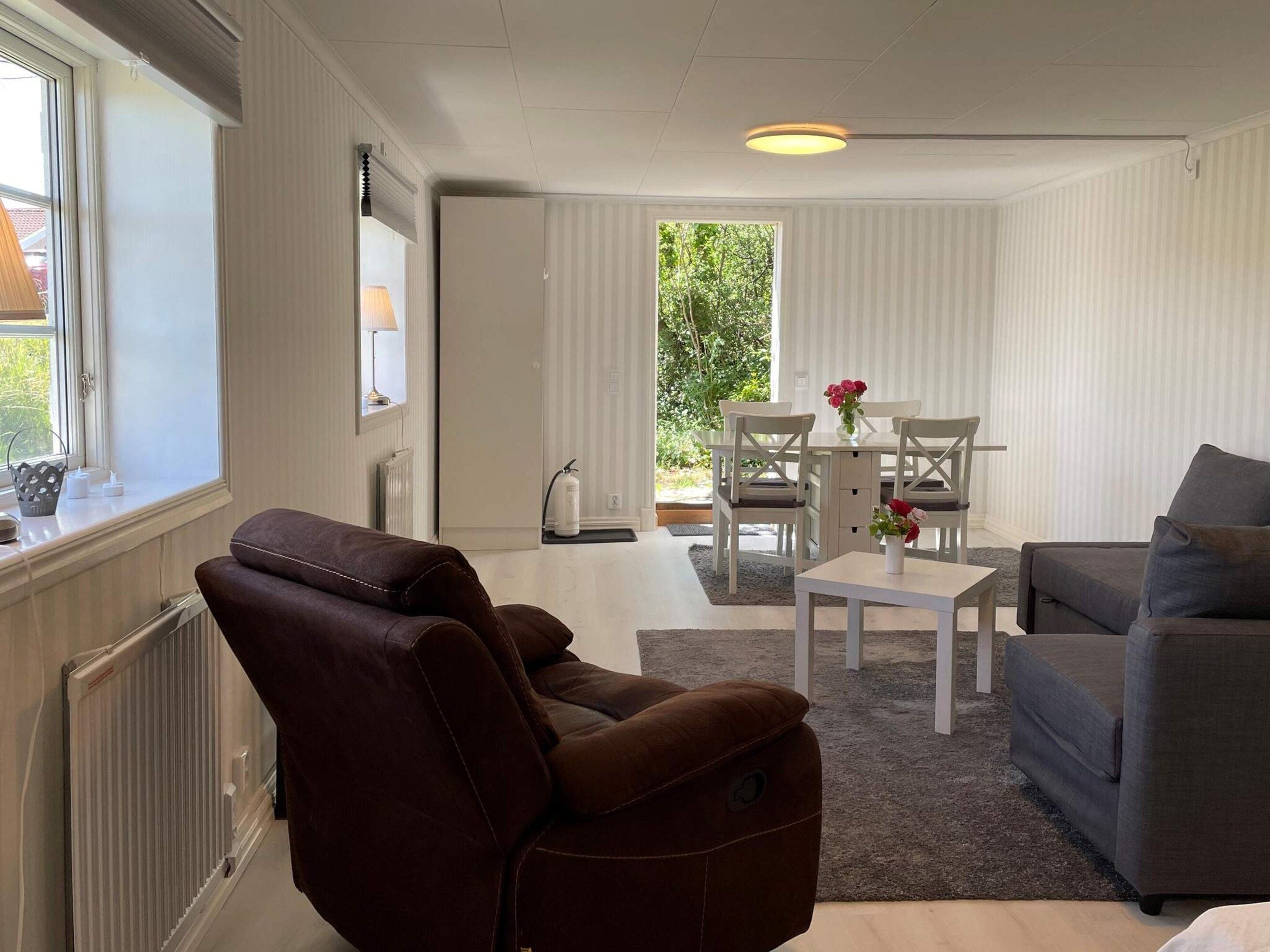Una sala de estar moderna con un sofá de cuero marrón, un sofá gris, una mesa de centro blanca y un comedor con sillas y una mesa blancos.