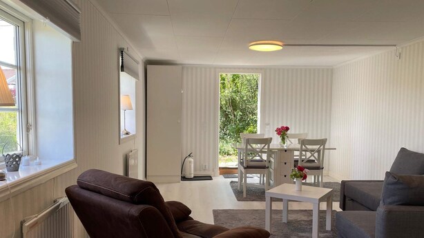 Ein modernes Wohnzimmer mit einem braunen Ledersofa, einem grauen Sofa, einem weißen Couchtisch und einem Essbereich mit weißen Stühlen und einem Tisch.