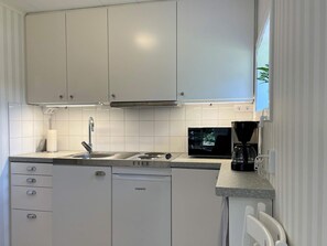 A compact kitchen with white cabinets, a stainless steel sink, a microwave, and a coffee maker. - 4 Star Holiday Home in Skarhamn (Skaerhamn)