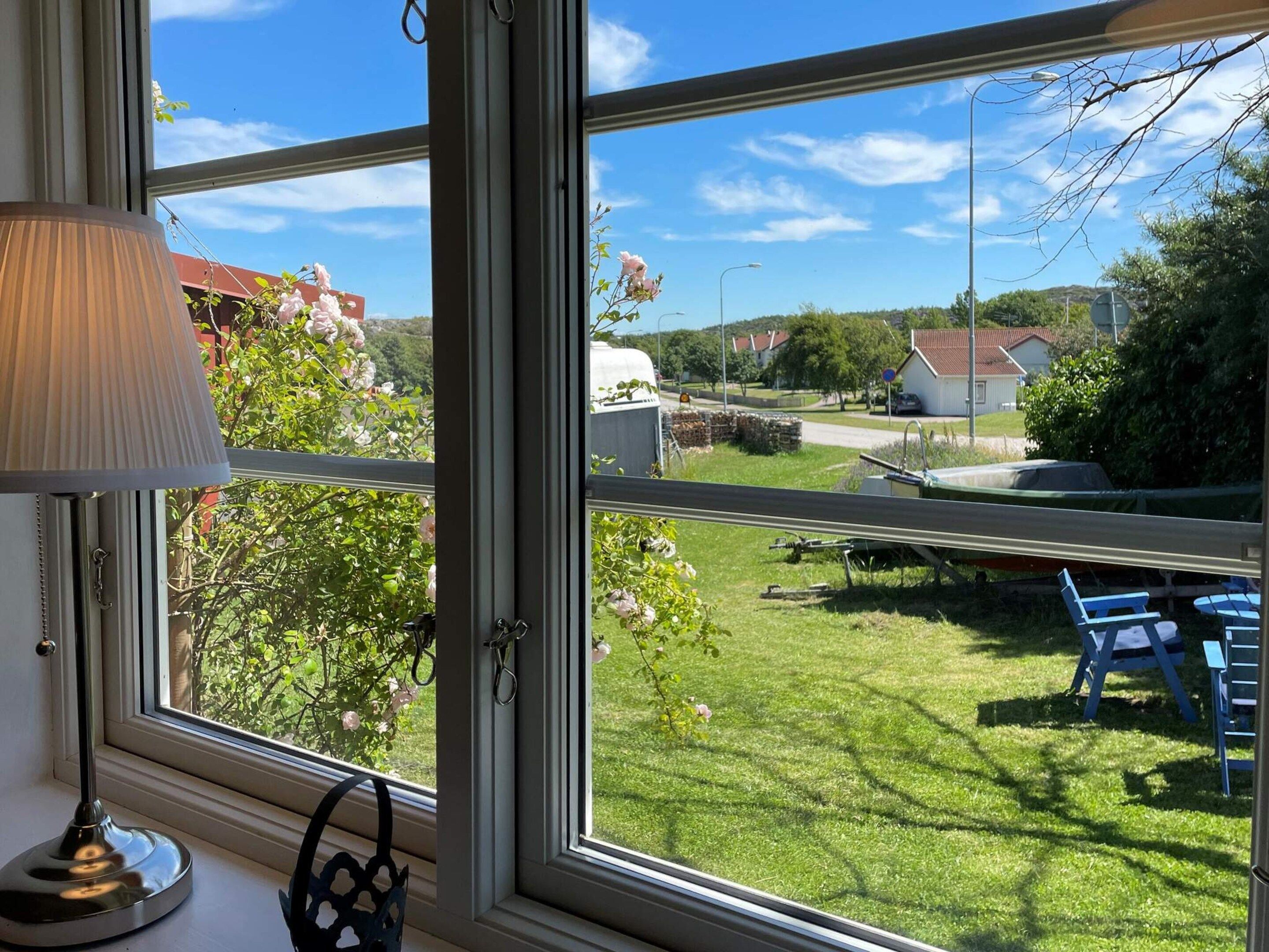 A room with a large window overlooking a grassy yard with a table and chairs, a lamp on the windowsill, and a bag.
