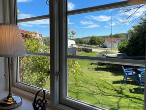 A room with a large window overlooking a grassy yard with a table and chairs, a lamp on the windowsill, and a bag. - 4 Star Holiday Home in Skarhamn (Skaerhamn)