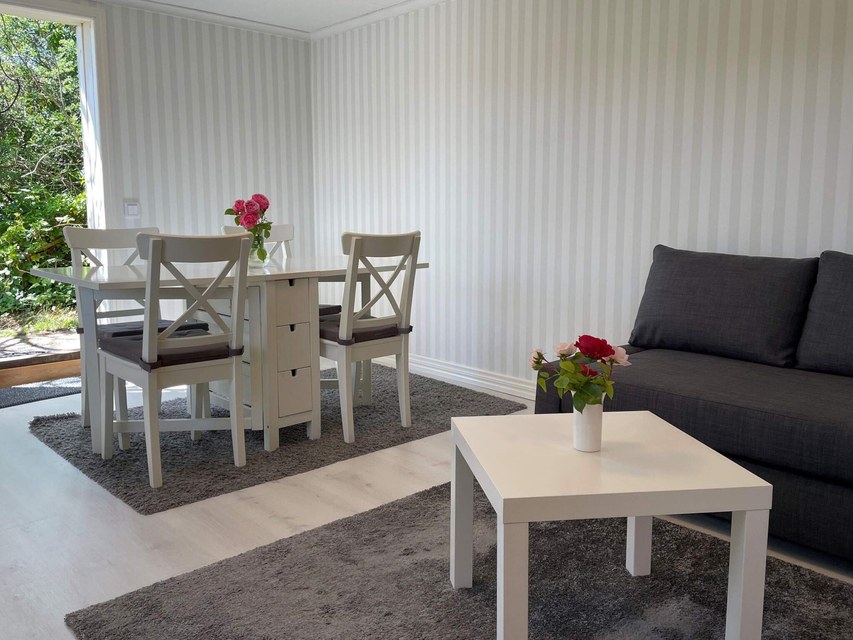 Una sala moderna con un sofá gris, una mesa de centro blanca y una mesa de comedor con sillas.