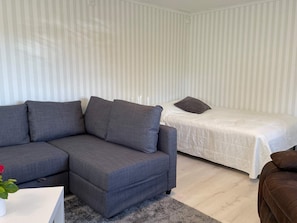 A modern living room with a grey sofa, a small white table with a vase, and a bed with a white mattress and brown pillow. - 4 Star Holiday Home in Skarhamn (Skaerhamn)