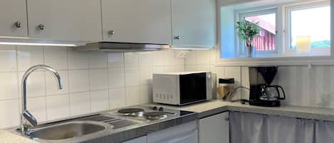 Una cocina con armarios blancos, un lavamanos de acero inoxidable, un microondas y una cafetera.