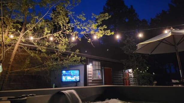A nighttime outdoor area with a hot tub, string lights, and a television screen. - Beautiful Cabin in Unbeatable Location (Pinetop-Lakeside)