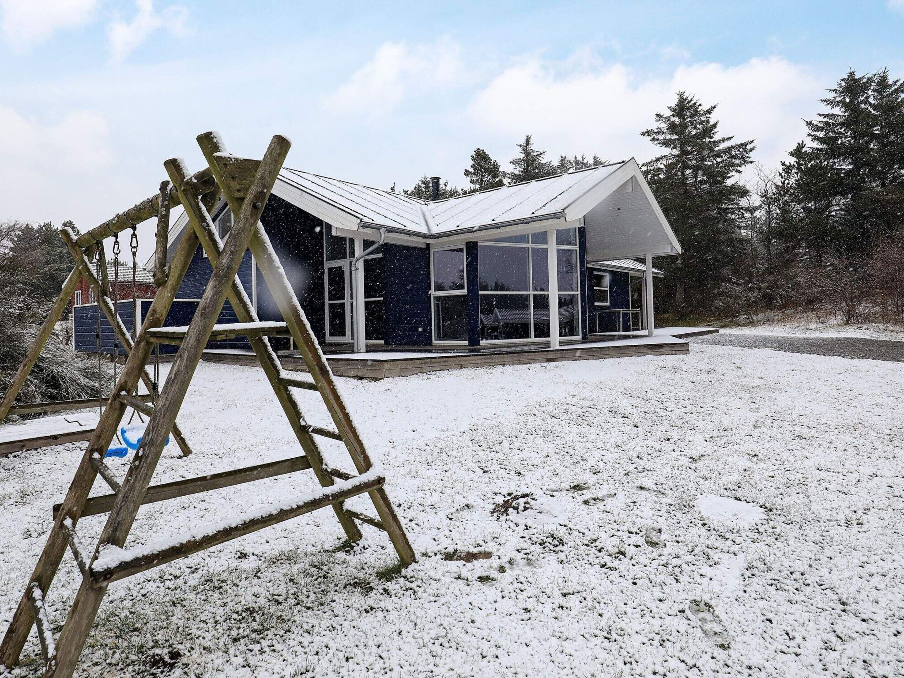 A modern house with a large glass window, a wooden ladder, and a snowy landscape.