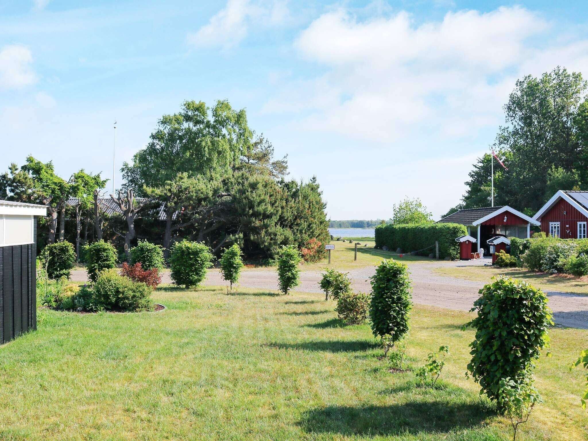 A grassy area with a small building, a large tree, and a body of water in the background.