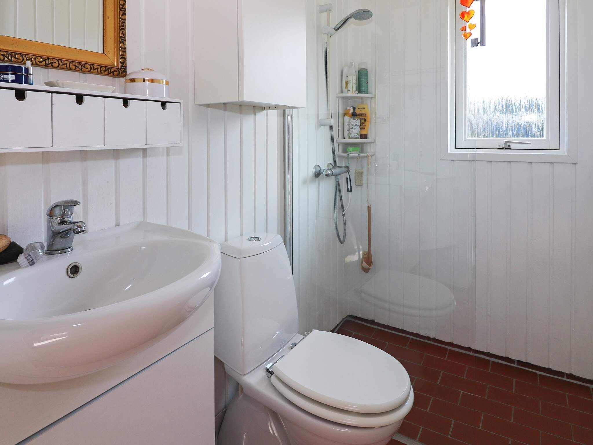 A bathroom with a white sink, toilet, and shower. There is a window with a view of the outside.