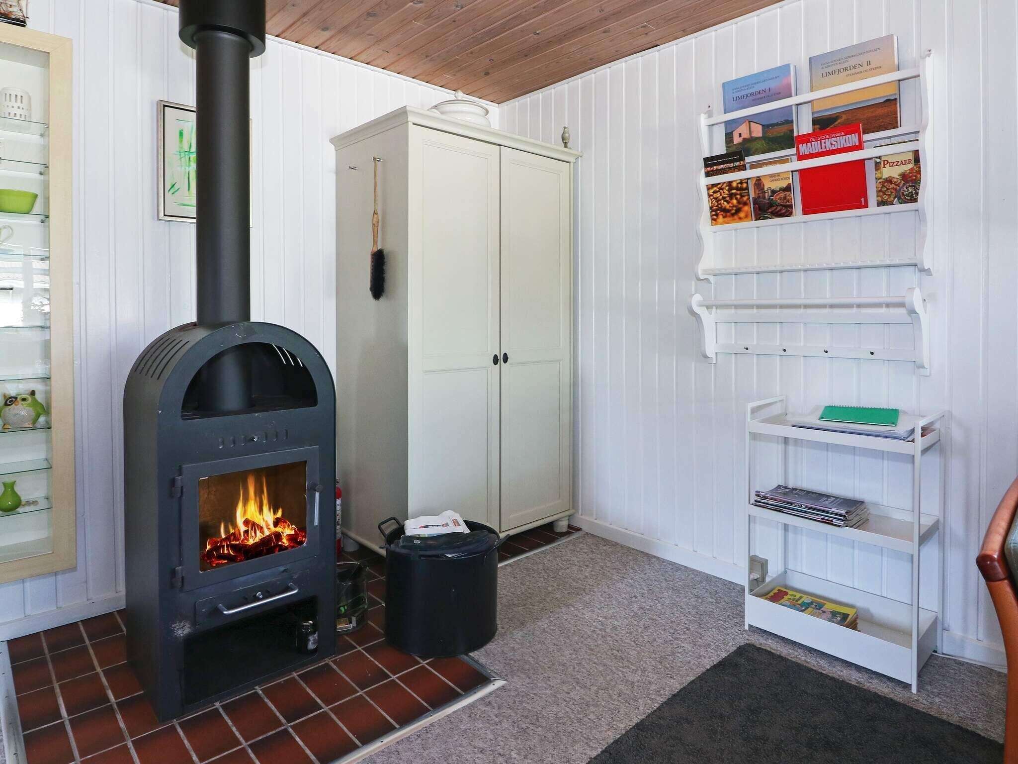 A room with a wood-burning stove, a white cabinet, and a shelf with books and magazines.