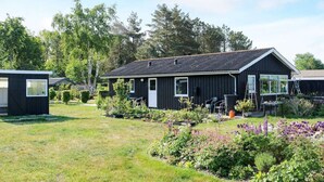 Una casa de madera negra con techo inclinado, rodeada de un jardín bien cuidado con diversas plantas y flores.
