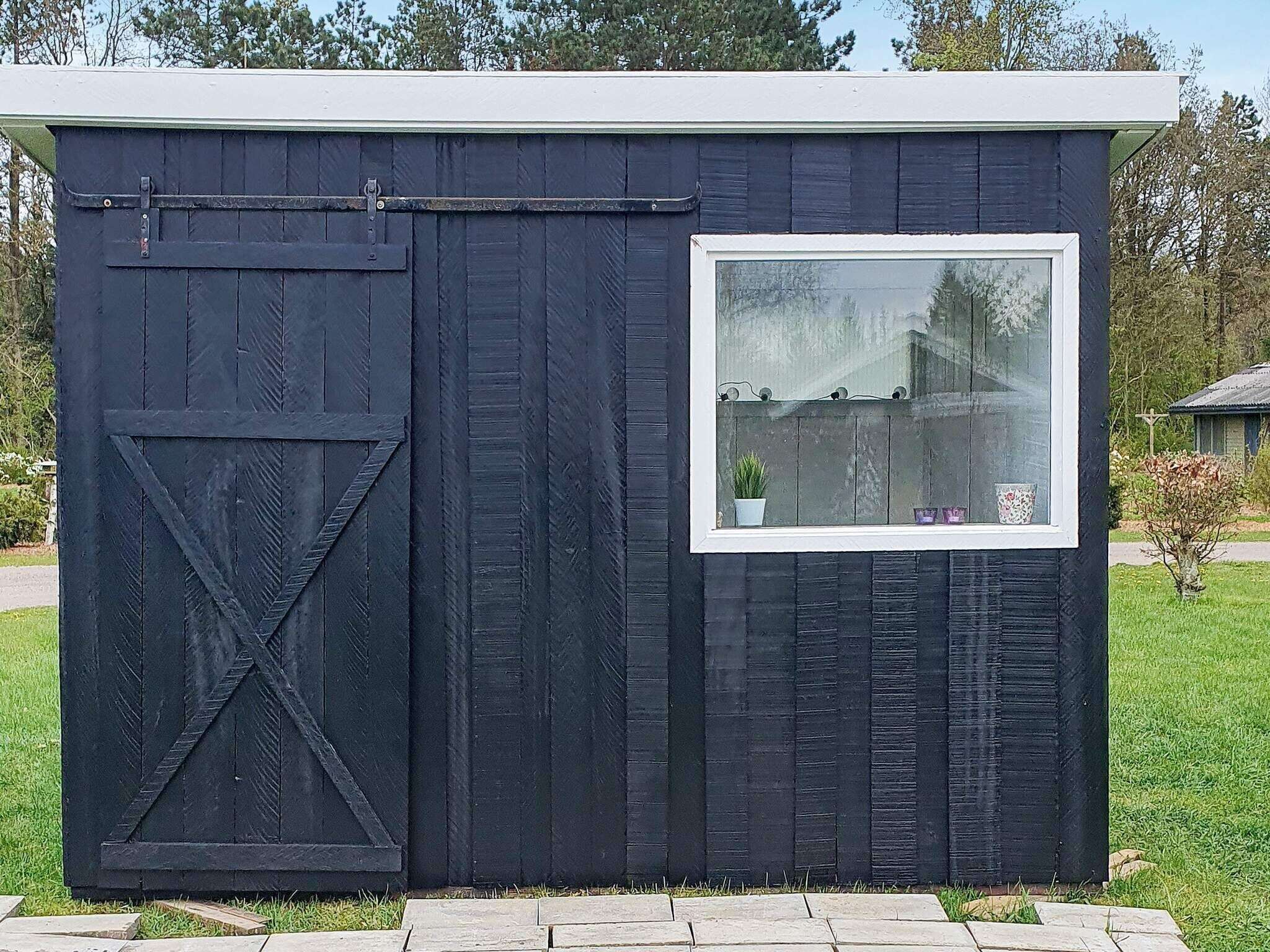 A small, dark wooden shed with a sliding door and a window.