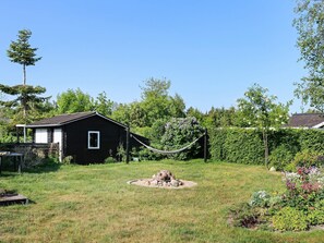 A black cabin with a small porch, surrounded by a grassy yard and a hammock. - 4 Person Holiday Home in Storvorde (Storvorde)