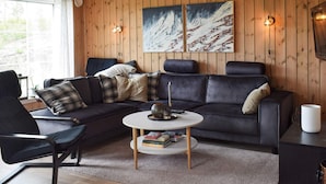 A modern living room with a dark leather sofa, a round coffee table, and a wooden wall with two paintings.