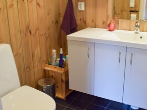 A bathroom with a wooden wall, a white sink, and a mirror. There is a small wooden shelf with toiletries. - 7 Person Holiday Home in Nesbyen (Nes)