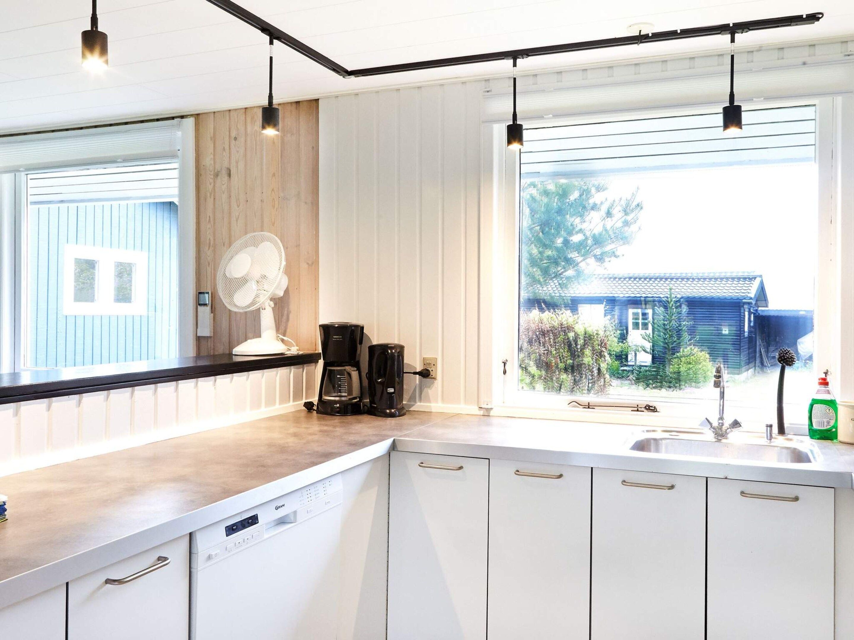 Cozinha moderna com máquina de lavar louça embutida, cafeteira e janela com vista para uma casa.