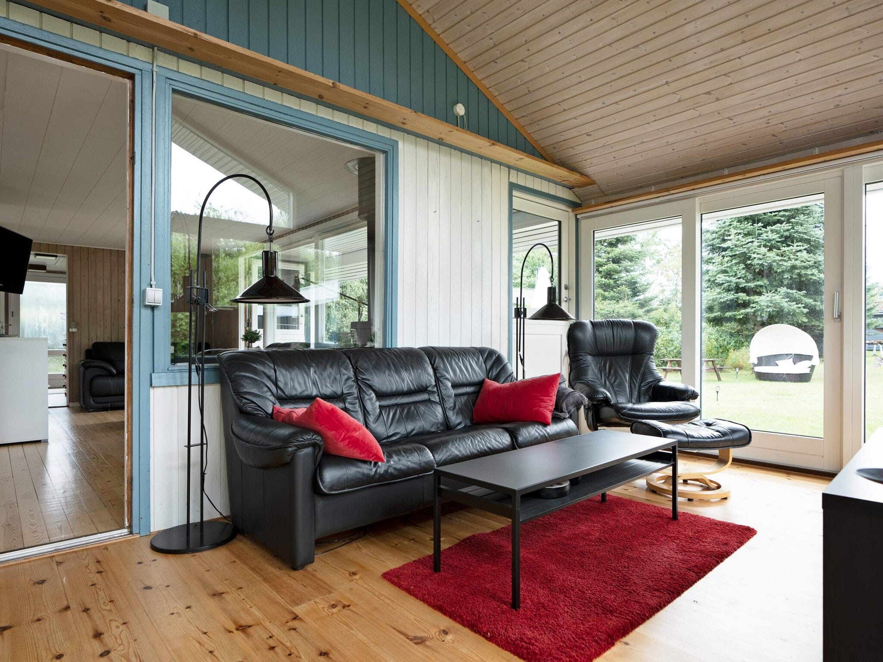 Uma sala de estar moderna com um sofá de couro preto, um tapete vermelho e piso de madeira.