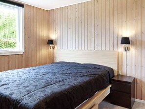 Une chambre à coucher avec un lit, des murs en bois, deux lampes fixées au mur et une fenêtre.