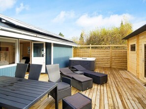 A covered outdoor patio with a hot tub, wicker furniture, and a wooden deck.