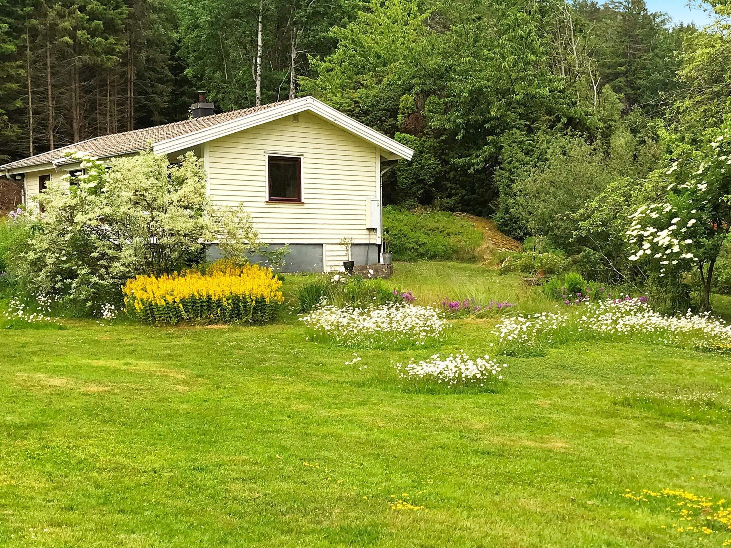 Une maison de plain-pied, dotée d’un toit en pente, entourée d’un jardin bien entretenu où poussent différentes plantes à fleurs et une pelouse.