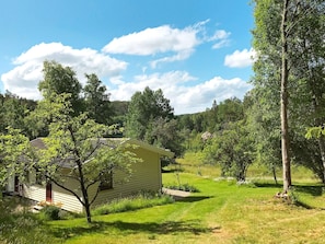 A single-story house with a sloped roof, surrounded by a grassy yard and trees.