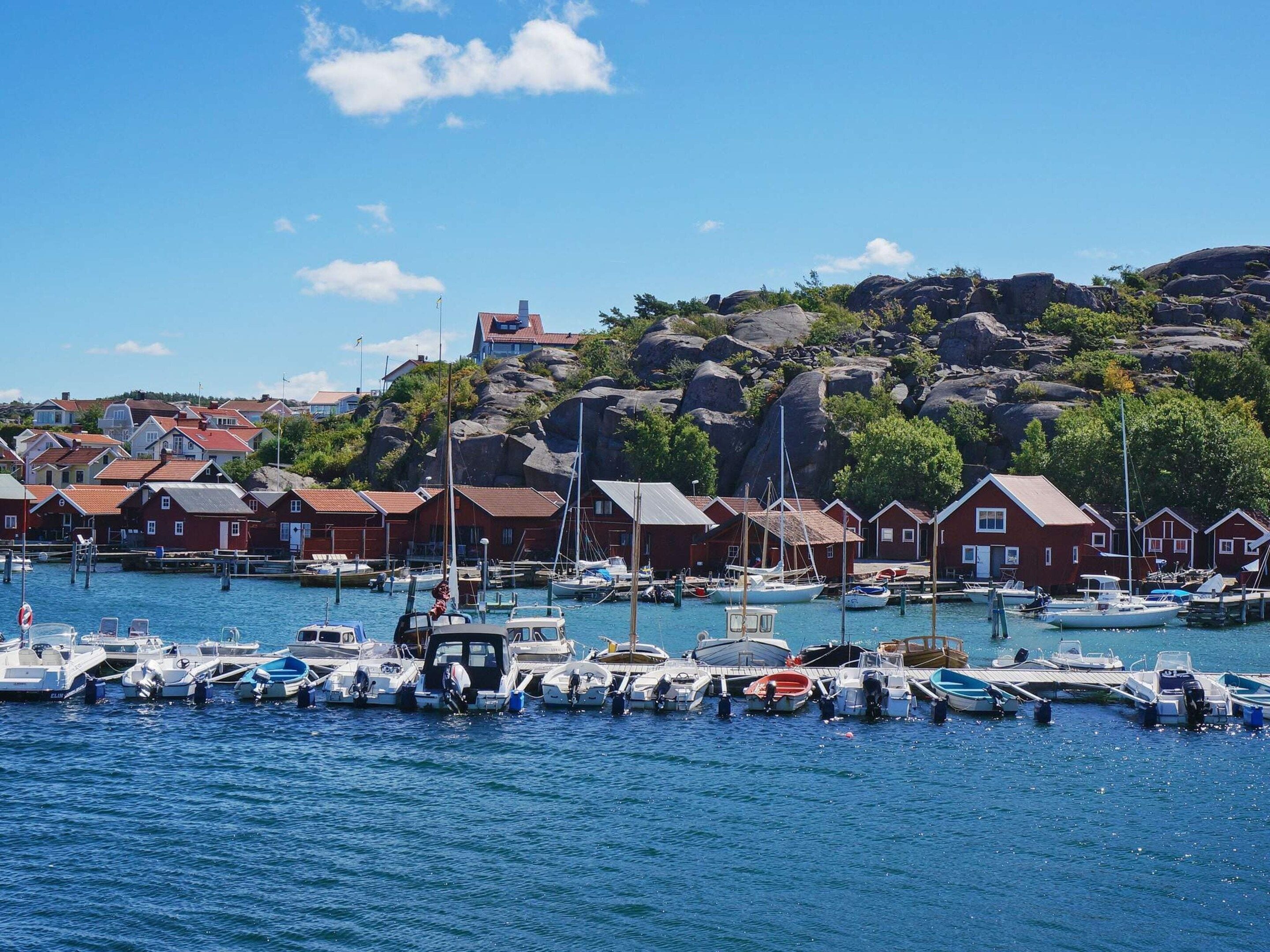 A harbor with boats docked, red houses, and rocky hills in the background.