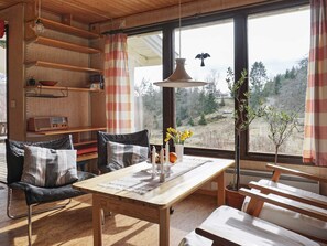 Una habitación acogedora con una mesa de madera, un sofá y una ventana que da a árboles y un sendero.